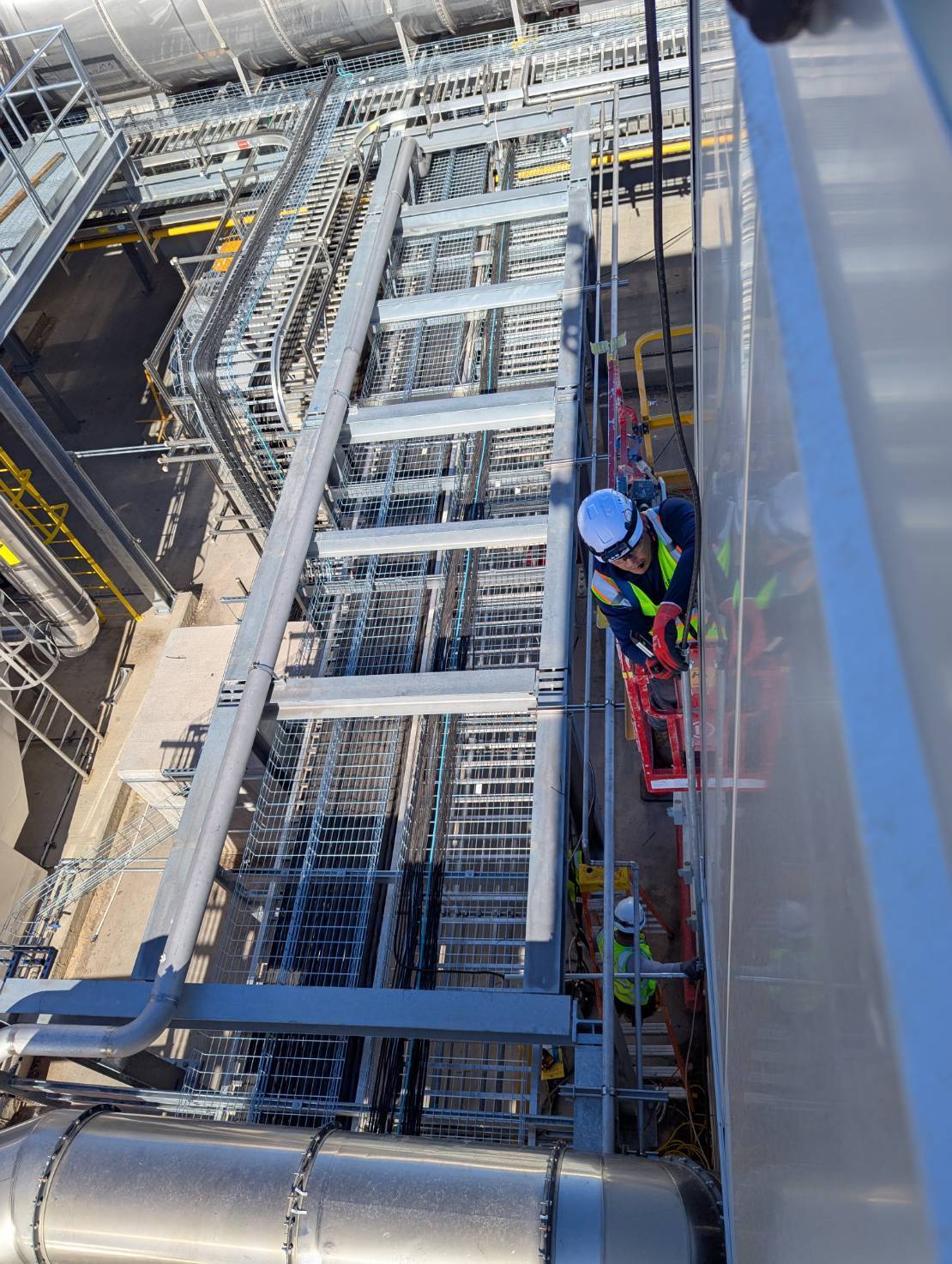 Overhead cable tray and conduit being dressed from a lift at the hall perimeter