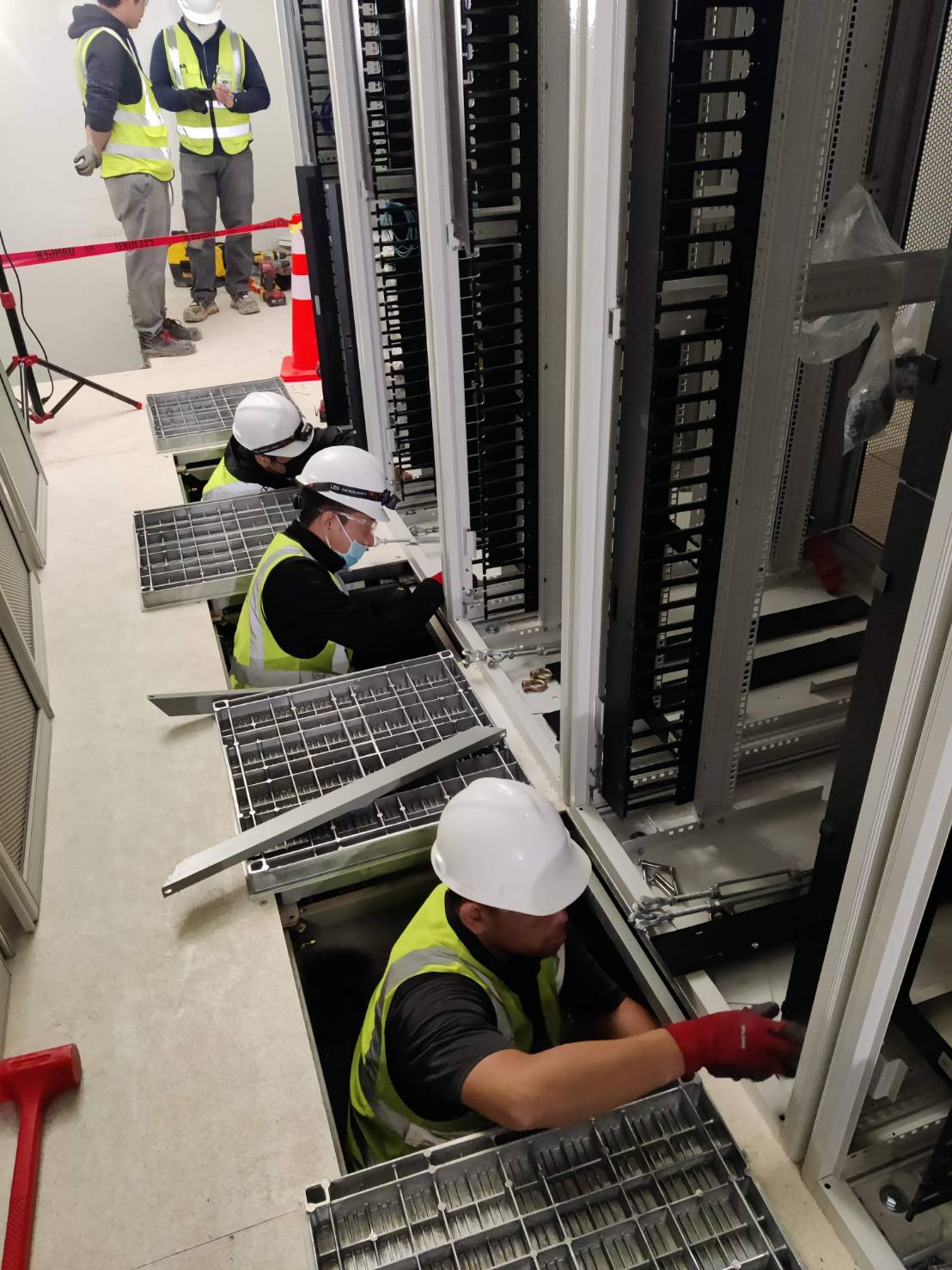 Technicians installing a server cabinet from the raised floor plenum